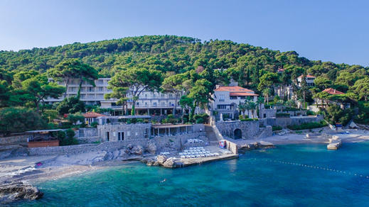 Luftaufnahme eines Hotels am Meer mit baumbewachsenen Hügeln im Hintergrund
